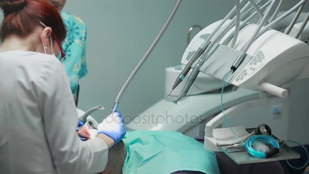 De tandarts en verpleegkundige herstellen van een tand van een geduldige man. Het gebruik van bormashenko om te boren tanden en verwijderen van tandbederf en afdichting. — Stockvideo