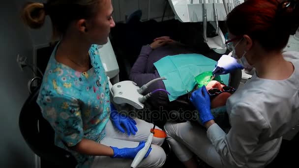 Female dentist and her nurse set the seal to the patient lying in the chair of a dental office. — Stock Video