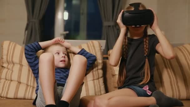 Bratr se sestrou doma sedí na gauči hraje hru pomocí virtuální realita brýle. Šťastná rodina — Stock video