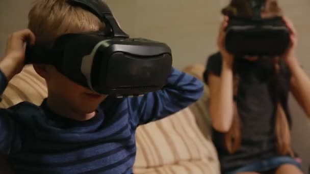 Брат с сестрой дома, сидят на диване и играют в игру, используя очки виртуальной реальности. Счастливая семья — стоковое видео