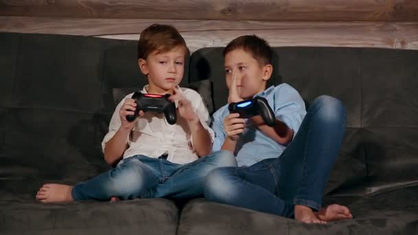 Zwei Brüder sitzen auf der Couch und spielen sehr emotional Videospiele mit kabellosem Steuerknüppel. — Stockvideo