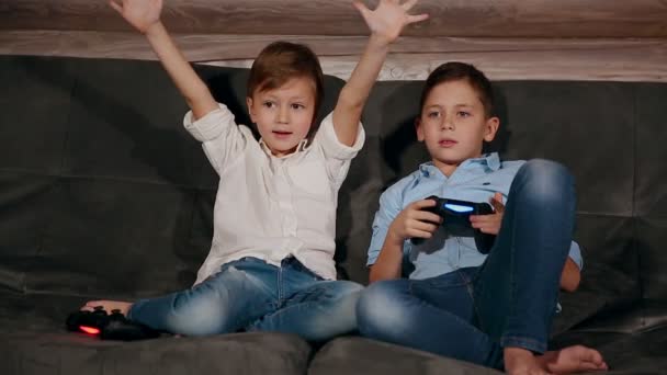 Два брата сидят на диване и очень эмоционально играют в видеоигры с беспроводным джойстиком . — стоковое видео