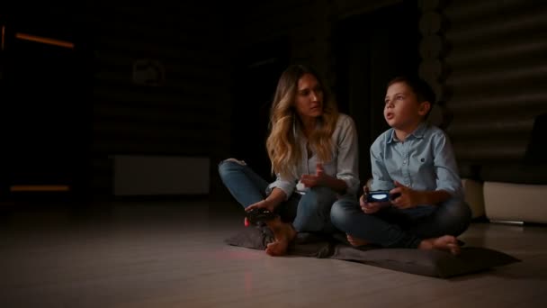 Bela mãe com seu filho jogando videogames no console de jogos na sala de estar de sua casa. Família feliz em uma casa de campo . — Vídeo de Stock