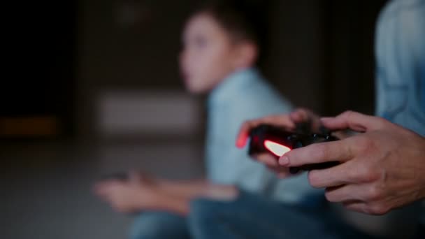 Руки тримають контролер на ігровій консолі, а на задньому плані хлопчик дивиться на кран і грає у відеоігри. Фокус змінюється від одного до іншого . — стокове відео
