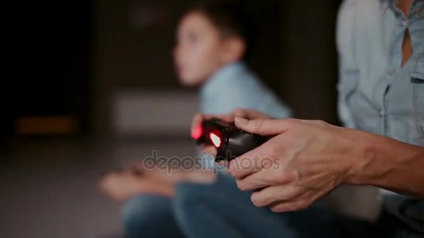 Руки держат контроллер к игровой консоли, а на заднем плане мальчик смотрит на кран и играет в видеоигры. Фокус смещается от одного к другому . — стоковое видео