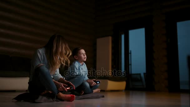 Όμορφη μητέρα με τον γιο της παίζοντας βιντεοπαιχνίδια στην κονσόλα παιχνιδιών στο σαλόνι του σπιτιού του. Ευτυχισμένη οικογένεια σε ένα εξοχικό σπίτι. — Αρχείο Βίντεο