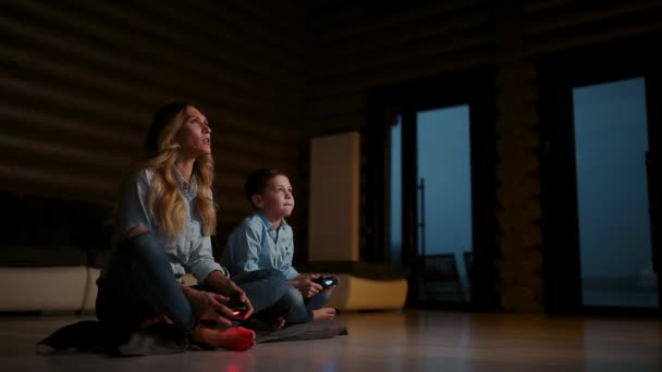 Bela mãe com seu filho jogando videogames no console de jogos na sala de estar de sua casa. Família feliz em uma casa de campo . — Vídeo de Stock