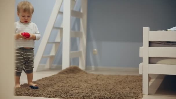 Un niño pequeño juega con juguetes y corre alrededor de la cámara en casa . — Vídeos de Stock