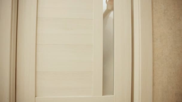 Niño en pijama jugando al escondite en casa con la puerta. Abre y cierra la puerta de la habitación. Primer plano . — Vídeo de stock