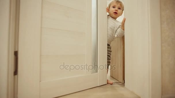 Menino de pijama em casa a brincar às escondidas com a porta. Abre e fecha a porta do quarto. Close-up . — Vídeo de Stock