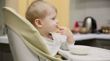 Küçük çocuk mutfakta ve tabakaları gelen çocuk koltuğunda oturan çok lezzetli yiyecek var. Gülümsüyor ve o dönemin oyunları.