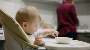 Küçük çocuk mutfakta ve tabakaları gelen çocuk koltuğunda oturan çok lezzetli yiyecek var. Gülümsüyor ve o dönemin oyunları.