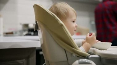Küçük çocuk mutfakta ve tabakaları gelen çocuk koltuğunda oturan çok lezzetli yiyecek var. Gülümsüyor ve o dönemin oyunları.