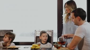 Dört büyük pencereler ile onun mutfakta kahvaltı aile. İnsanların gülümseyen, öpüşme ve çocuklar anne. Anne baba ve iki çocuk.