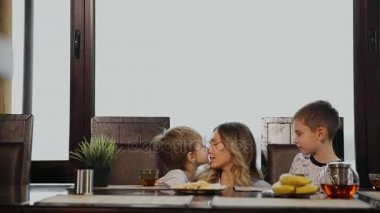 Sarılma ve onların çocukları mutfakta kahvaltı için öpüşme anne. Çocuklar gülüyor.