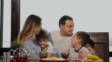 Dört büyük pencereler ile onun mutfakta kahvaltı aile. İnsanların gülümseyen, öpüşme ve çocuklar anne. Anne baba ve iki çocuk.