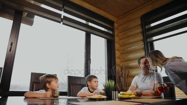 Familj på fyra med frukost i hans kök med stora fönster. Människor ler, mor kyssas och kramas barn. Mor far och två barn. — Stockvideo