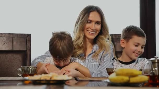 Η μητέρα αγκαλιάζει και φιλιά στα παιδιά τους για πρωινό στην κουζίνα. Τα παιδιά το γέλιο. — Αρχείο Βίντεο