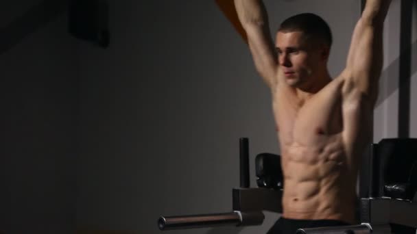 Un hombre con un torso desnudo se sienta-UPS con los aumentos de pierna en la barra horizontal en el gimnasio . — Vídeos de Stock