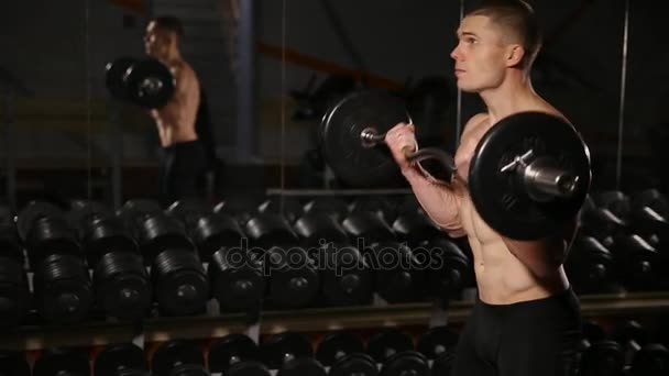 Hombre guapo con grandes músculos, posando en el gimnasio hombre musculoso levantando pesas sobre fondo oscuro hombre musculoso haciendo ejercicio en el gimnasio haciendo ejercicios con barra en bíceps hombre fuerte. primer plano — Vídeo de stock