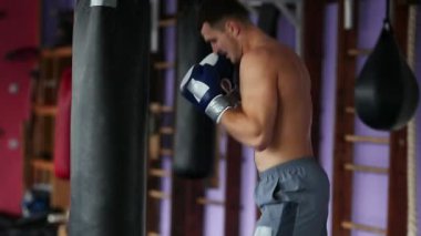 Kum torbası spor salonunda boks eldivenleri çıplak göğüslü, kaslı erkek profesyonel boksör tren.