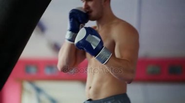 Kum torbası spor salonunda boks eldivenleri çıplak göğüslü, kaslı erkek profesyonel boksör tren.