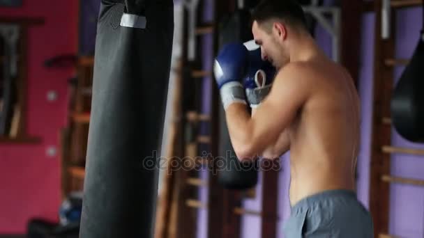 Masculino musculoso boxeador profesional entrena por saco de boxeo en el gimnasio en guantes de boxeo con el pecho desnudo . — Vídeo de stock