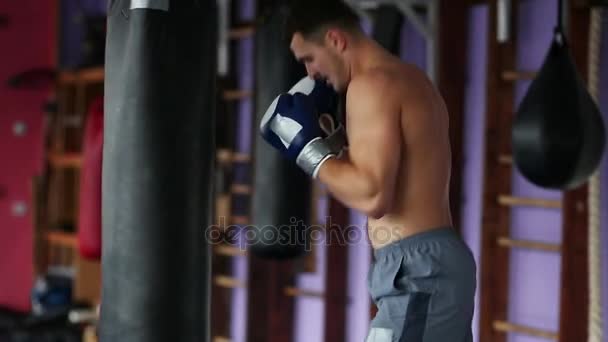 Мускулистый мужчина профессиональный боксер тренируется, пробивая грушу в тренажерном зале в боксёрских перчатках с голыми грудями . — стоковое видео
