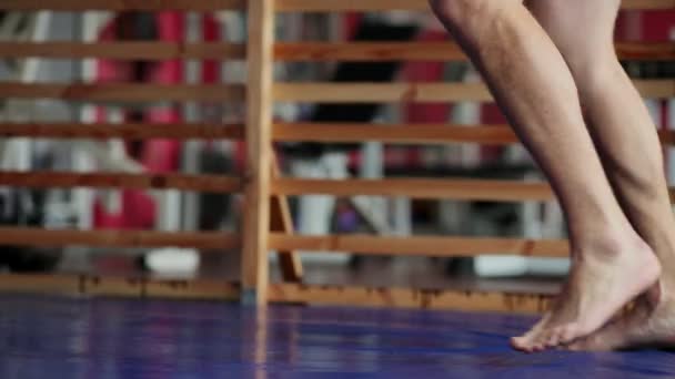Un boxeur professionnel mène des frappes sur le sac de boxe avec des gants de boxe à poitrine nue. Un mouvement de caméra verticale en gros plan. Pan. Les jambes du boxeur . — Video