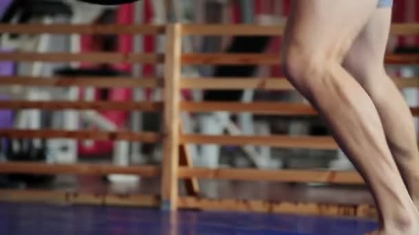 Un boxeur professionnel mène des frappes sur le sac de boxe avec des gants de boxe à poitrine nue. Un mouvement de caméra verticale en gros plan. Pan. Les jambes du boxeur . — Video