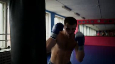 Kum torbası spor salonunda boks eldivenleri çıplak göğüslü, kaslı erkek profesyonel boksör tren.