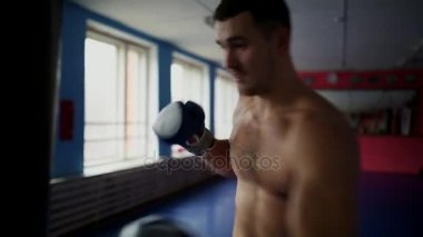 Kum torbası spor salonunda boks eldivenleri çıplak göğüslü, kaslı erkek profesyonel boksör tren.