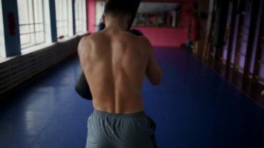Erkek boxer görünümünü arka çanta boks eldivenleri için yumruk spor salonunda yapar. Profesyonel boksör için çıplak göğüslü boks eğitimi yürütmektedir. Yakın çekim.