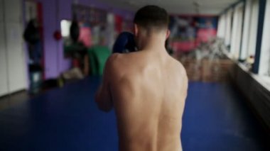 Erkek boxer görünümünü arka çanta boks eldivenleri için yumruk spor salonunda yapar. Profesyonel boksör için çıplak göğüslü boks eğitimi yürütmektedir. Yakın çekim.