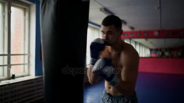 Masculino musculoso boxeador profesional entrena por saco de boxeo en el gimnasio en guantes de boxeo con el pecho desnudo . — Vídeos de Stock