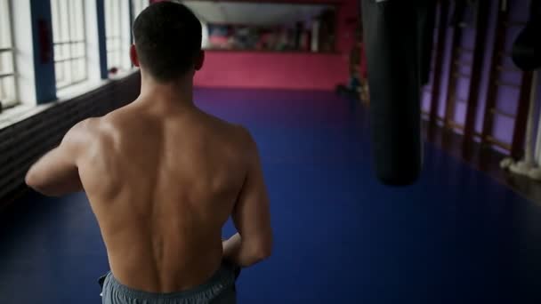 Visão traseira do boxeador masculino faz socos para luvas de boxe saco no ginásio. boxeador profissional realiza treinamento para Boxe de peito nu. Close-up . — Vídeo de Stock