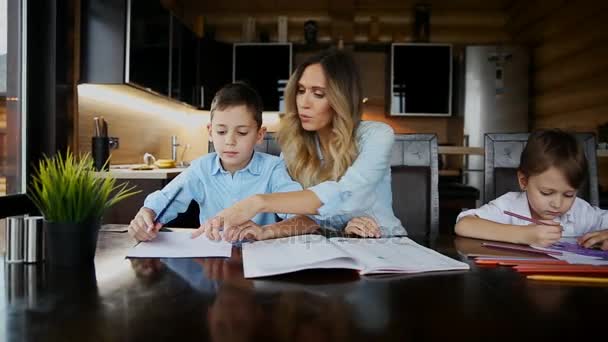 두 아이의 행복 가족 어머니 도움이 부엌 큰 테이블에 앉아 그들의 숙제를 할 아들. — 비디오