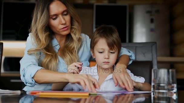 Όμορφη μητέρα βοηθάει το γιο της για να ζωγραφίσετε με χρωματιστά μολύβια εικόνας. Βοηθώντας να αναπτύξουν μια φαντασία του παιδιού. — Αρχείο Βίντεο