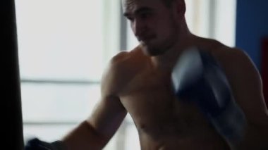 Kum torbası spor salonunda boks eldivenleri çıplak göğüslü, kaslı erkek profesyonel boksör tren.