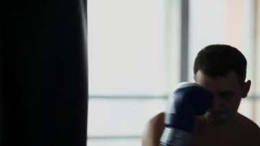 Kum torbası spor salonunda boks eldivenleri çıplak göğüslü, kaslı erkek profesyonel boksör tren.