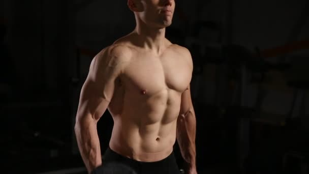 Atlético sin camisa joven deportista modelo de fitness sostiene la mancuerna en el gimnasio. Primer plano — Vídeo de stock