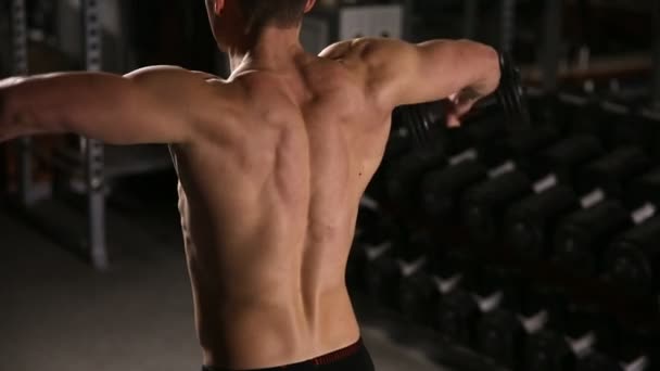 Uomo laminato con muscoli increspati che eseguono esercizi per le spalle con manubri in palestra . — Video Stock