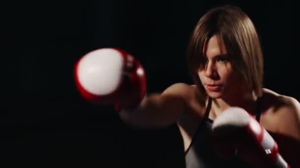 Brunette in sport suit and Boxing gloves on a black background conducts training punches in the air. Shadow Boxing. Close-up — Stock Video