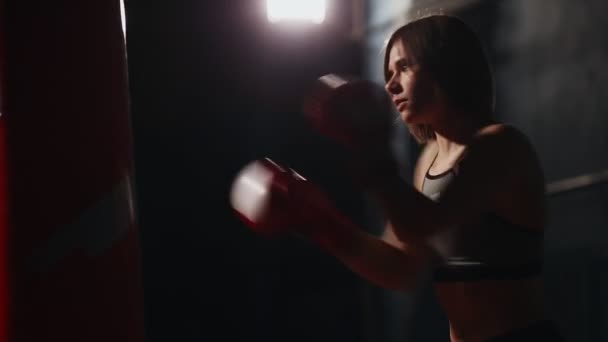 Die sportliche brünette Boxgymnastik bietet individuelles Training in Schlagtechnik. Schläge auf einen Boxsack vor schwarzem Hintergrund. — Stockvideo