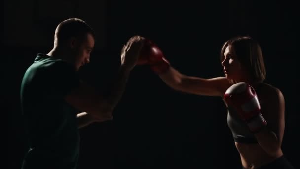 Fata de fitness musculară se antrenează cu instructorul său pentru a efectua greve pe picioare în mănuși de box. Lecţia autoapărării. Un antrenament de box . — Videoclip de stoc