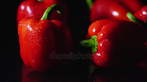 Pimientos rojos frescos gotas recién lavadas fluyen hacia abajo sobre la mesa. Primer plano girando sobre fondo negro . — Vídeo de stock