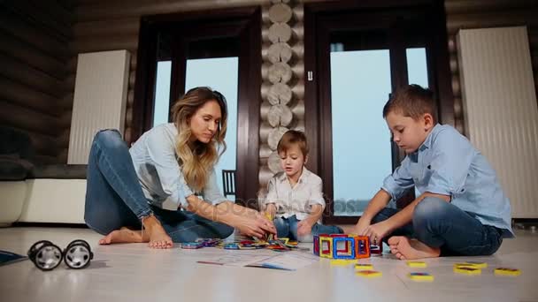 Madre feliz con dos niños sentados en el suelo de su casa de campo pasar tiempo juntos coleccionando diseñador de niños. Salón con ventanas panorámicas . — Vídeos de Stock