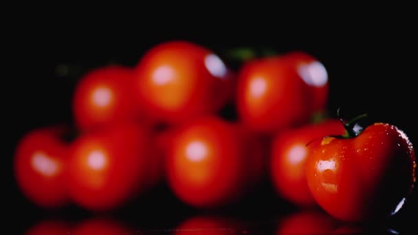 Fresh washed tomatoes are on the surface on a black background. Close-up of a drop of water flows over the surface of the vegetables. — Stock Video