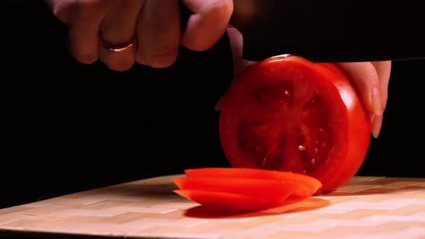 Weibliche Hand in Großaufnahme nimmt das Messer und Scheiben reifer Tomaten auf einem Schneidebrett vor schwarzem Hintergrund. — Stockvideo