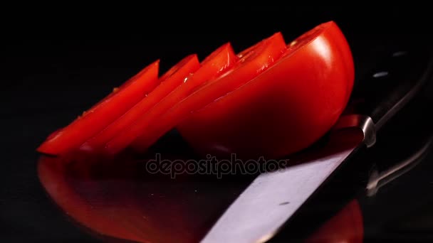 Reife Tomaten in Scheiben geschnitten, dazu ein rotierendes Messer auf einem schwarzen Tisch vor schwarzem Hintergrund. — Stockvideo